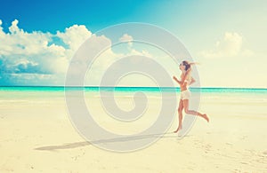 Young woman running on summer beach on coast of the ocean