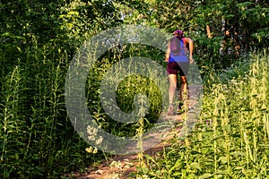 Young woman is running uphills in forest, evening sunlight