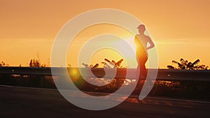 A young woman runs along the road along the seashore at sunset. Silhouette of an unrecognizable person