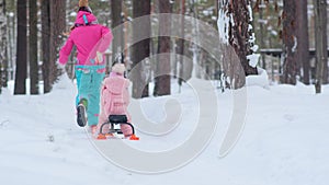 Young woman runs along white snowy forest path carrying sled