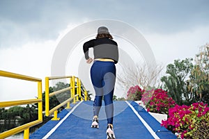 A young woman runs up a hill on a pedestrian bridge over a canal