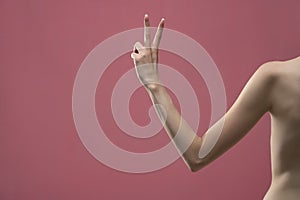 Young woman`s arm showing two fingers. Isolated on pink background