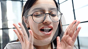 A young woman's face in close-up with glasses in the office, she is surprised