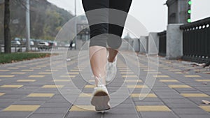 Young woman`s feet in white professional running sneakers doing intense training on city quay along river. Sports woman athlete ru