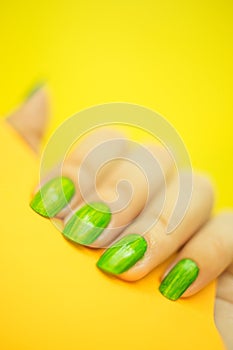 Young woman`s hand with beautiful manicure on yellow background holding orange color paper