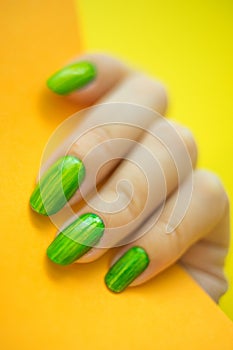 Young woman`s hand with beautiful manicure on yellow background holding orange color paper close up