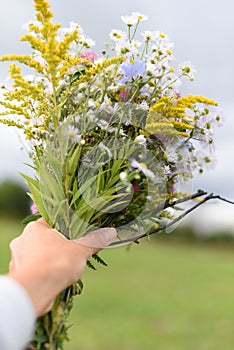 A young woman`s hand holding a bouquet of colorful field flowers