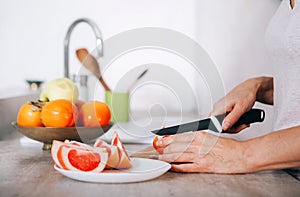 Young woman`s hands chopping grapefruit using a knife and cutting board in modern kitchen close up image. Plenty of apples,