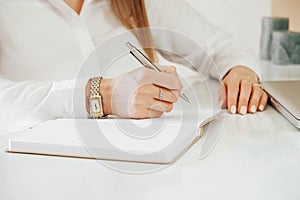 Young woman`s hands holding pen and writing. Close up of lady`s hand writing in notepad placed on desktop with other items