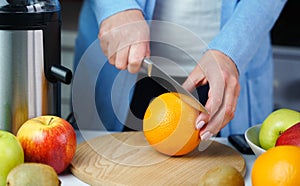 Young woman`s hands with a knife cut an orange for making fresh juice at the kitchen. Healthy or dietary food concept. Close-up