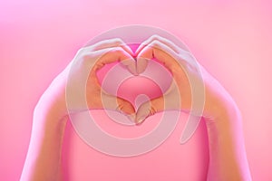 Young woman`s hands made gesture of heart shape in trendy neon light.