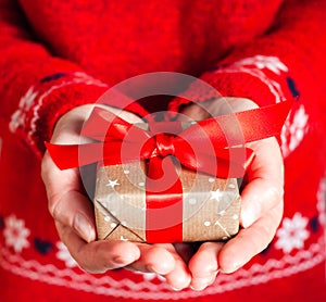 Young woman`s hands in red pullover holding gift box with red ribbon. Close-up. Holiday gift. Christmas, New Year, Valentine`s d