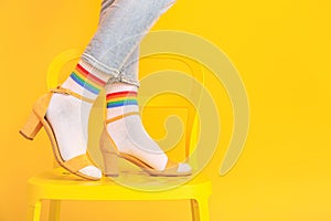 Legs of young woman in socks and sandals standing on chair against color background