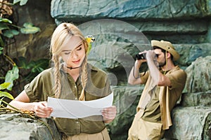 young woman in safari suit with parrot and map navigating in jungle while her boyfriend