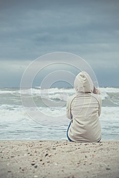 Young woman on the sand beach and watching the sea waves