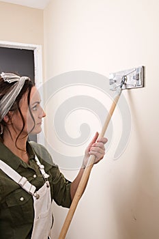 Young woman is sanding wall with pole sander before painting