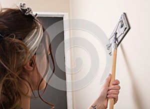 Young woman is sanding wall with pole sander before painting