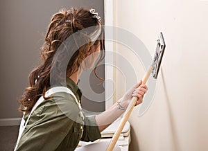 Young woman is sanding wall with pole sander before painting