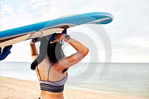 Young woman on the sandy beach carries a surfboard on her head