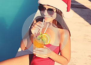 Young woman in Santa Claus hat with refreshing drink near swimming pool. Christmas vacation