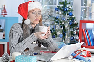 Young woman in Santa hat with cup of tea sitting in front of laptop