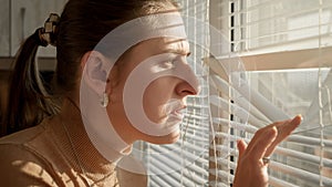 Young woman saw crime happening on street through window blinds. Crime witness, spying through window, peeking on street