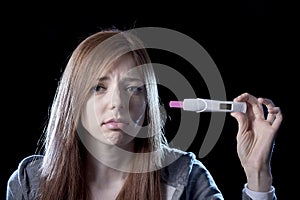 Young woman scared and shocked holding pregnancy test positive result looking unhappy