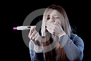 Young woman scared and shocked holding pregnancy test positive result looking unhappy