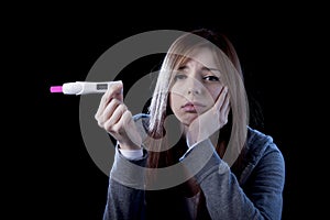 Young woman scared and shocked holding pregnancy test positive result looking unhappy