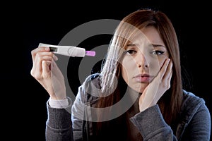 Young woman scared and shocked holding pregnancy test positive result looking unhappy