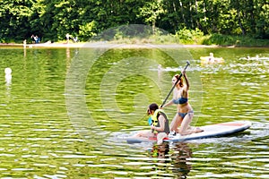 Young woman with school girl paddling on sup board on a lake. Active family on modern trendy stand up paddle board