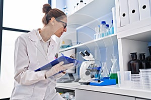 Young woman scientist measuring liquid writing on clipboard at laboratory