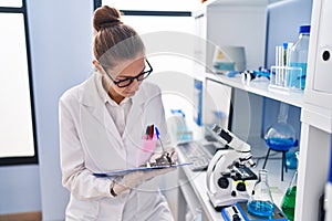 Young woman scientist measuring liquid writing on clipboard at laboratory