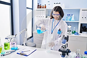 Young woman scientist pouring liquid on test tube at laboratory
