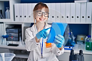 Young woman scientist smiling confident using touchpad at laboratory