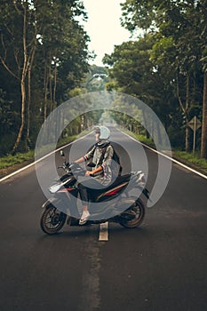 Young woman on the scooter on the road among the trees. Bali island.