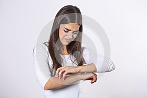 Young woman scratching her arm due to itching on a gray background. Female has an itching arm. The concept of allergy symptoms and