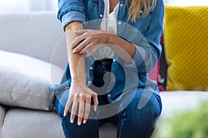 Young woman scratching her arm while sitting on the sofa at home