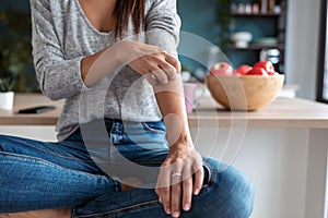 Young woman scratching her arm while sitting on the stool in the home kitchen