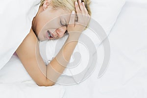 Young woman screaming while suffering from headache in bed