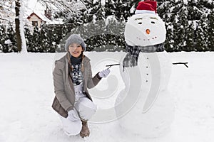 A young woman sculpts a snowman in her yard