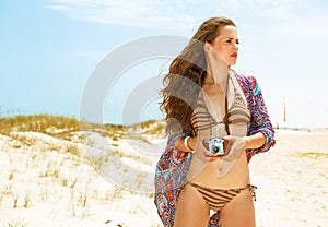 Young woman on seacoast with retro film camera looking aside