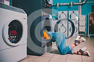 Young woman searching clothes in washing machine drum at laundromat.