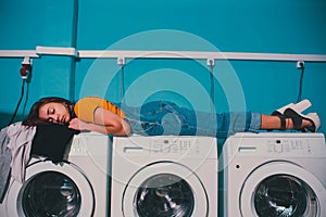 Young woman searching clothes in washing machine drum at laundromat.