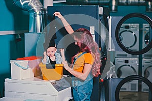 Young woman searching clothes in washing machine drum at laundromat.