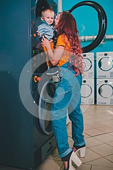 Young woman searching clothes in washing machine drum at laundromat.