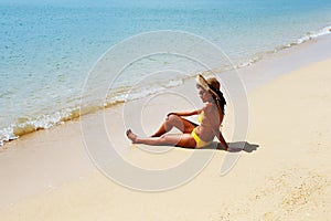 Young woman seating down on a sandy beach and sun bathing