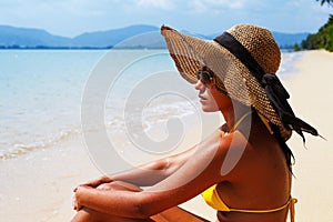 Young woman seating down on a sandy beach and sun bathing