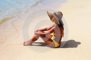 Young woman seating down on a sandy beach and sun bathing