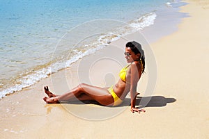 Young woman seating down on a sandy beach and sun bathing